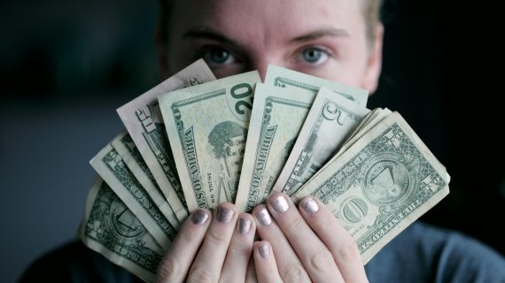 Woman holding fanned out money in front of her face.